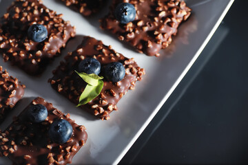 Chocolate dessert with nuts and fresh berries. Sweet snack for coffee biscuit in glaze and nut crumbs with fruit.