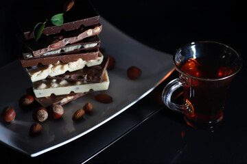 A bar of milk chocolate. Homemade milk chocolate with almonds and dried strawberries. Pieces of milk chocolate. Set of milk chocolate with tea.