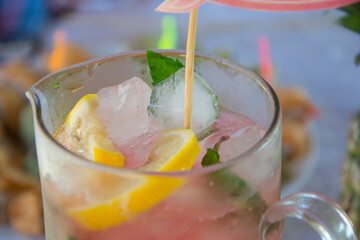 Pink melon lemonade or cocktail in a glass jar, with lemons, mint and ice and topper 