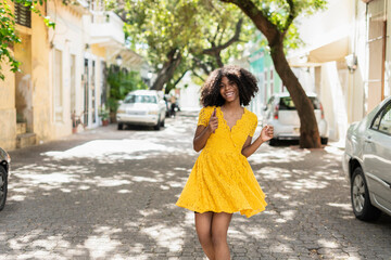 Young black woman with curly hair, in yellow dress and with styles, attitude, laughing, happy
