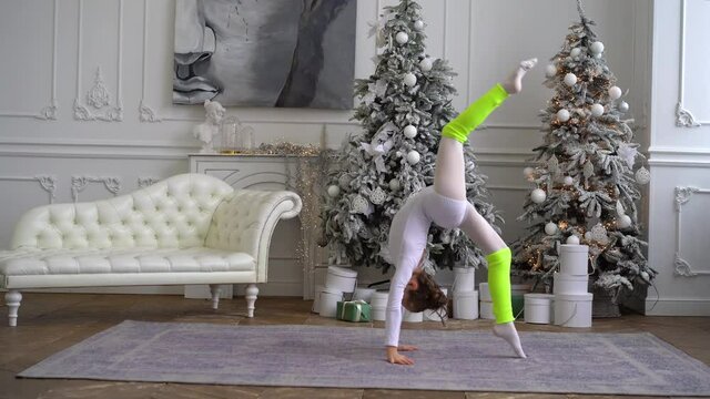 A little girl performs gymnastic exercises in a studio decorated for the New year