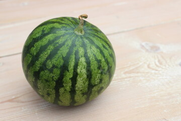 Green striped watermelon on wooden planks background.