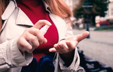 Closeup image of young adult woman using sanitizer or disinfectant spray walking the street....