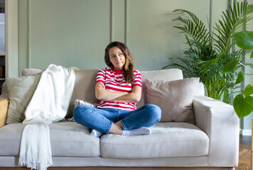 Young woman looking thoughtful while relaxing on the sofa at home.