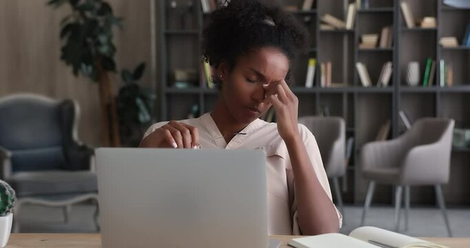 Tired african woman take off glasses resting from laptop work. American businesswoman suffers from dry irritable eyes after long notebook usage. Eye strain, conjunctivitis infection need drops concept