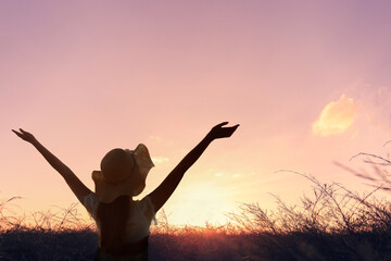The silhouette of a healthy woman raising her hand on a natural meadow blurred background