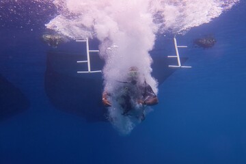 Scuba diver jumping in to the sea, the boat silhouette above him.