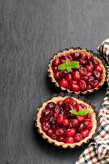 Delicious cranberry tarts in baking mold on black stone background