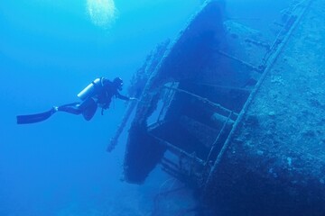Man scuba diver swimming near the ship wreck in blue deep water. Ship wreck SS Thistlegormm, Red sea Egypt.