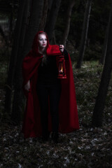 Attractive woman dressed a little red riding-hood walk in a dark forest with lantern