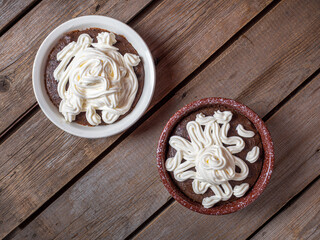 Two ceramic bowls with bread soup with whipped cream on a wooden table