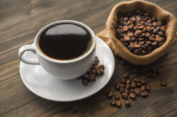 Cup of coffee with burlap sack of roasted beans on wooden table