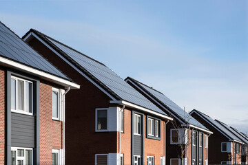 Solar panels mounted on the roofs of a row modern new-build houses in Lemmer, Friesland, the Netherlands with blue sky - obrazy, fototapety, plakaty