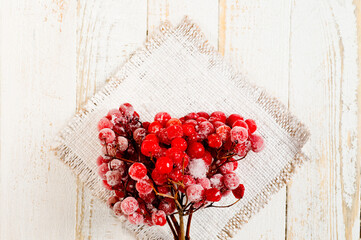 Twigs of ripe red viburnum frozen and sprinkled with snow, lying on a white wooden surface.