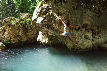 A woman in a swimsuit climbs a cliff above the water.