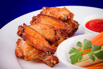 Roasted chicken wings with sticks carrots and celery and dipping sauce on white plate on blue background