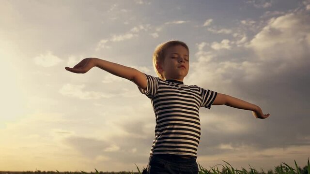 Happy kid praying in the park. Kid in a field with wheat praying raised his hands to the sides. Happy child closing his eyes looks to the sky. Child prays to the sky childhood dreams. Spiritual prayer