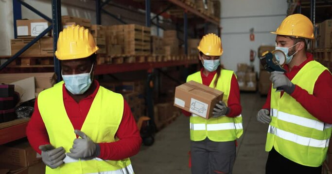 Happy workers dancing inside warehouse while wearing surgical masks during coronavirus outbreak