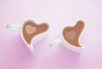 cappuccino or latte in white cups in the shape of a heart on a pink background, top view