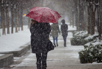 woman walks with red umbrella under the snow in madrid