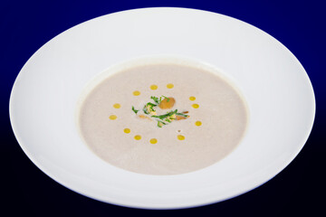 Creamy mushroom soup with herbs on a white plate and a blue background