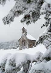 ZAVIŽAN, CROATIA, January 2021 - Votive chapel of Saint Ante in the Northern Velebit National park. Chapel is situated near botanical garden. View through spruce branches covered with snow.
