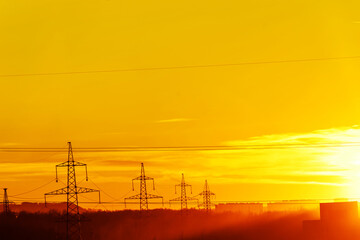 Fototapeta premium Power lines against the background of an orange sunset. Infrastructure of the city in beautiful sunshine. Copy space