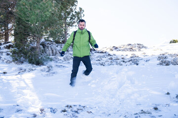 dark handsome man in green snow jacket running happily on top of a big snowy mountain