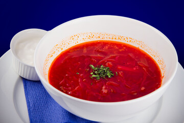 White bowl of traditional Ukrainian and Russian soup borsch or vegetable beetroot soup with sour cream on blue background