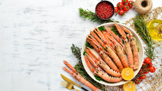 Boiled langoustines with parsley and spices on a plate. Norway lobster on a white wooden background. Top view. Free copy space.