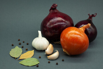 Composition of vegetables. Onions, garlic, bay leaves, and black pepper. Dark gray background.
