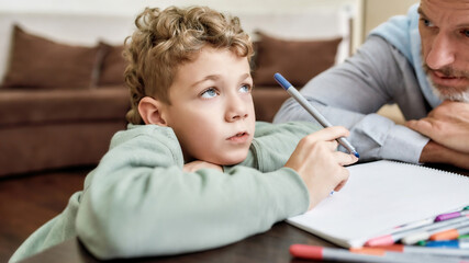Cute little boy grandson drawing with colored felt tip pens with his grandfather while sitting at...