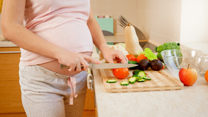 CLoseup of pregnant yougn woman cooking on kitchen and cutting fresh tomato. Concept of healthy lifestyle and nutrition during pregnancy