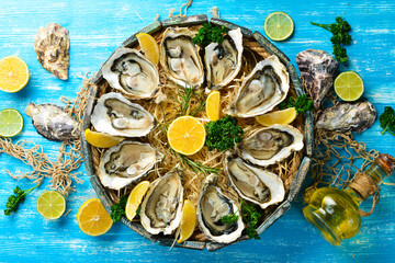 Open oysters in a wooden box on a blue wooden background. Free space for text. Top view. Flat lay.
