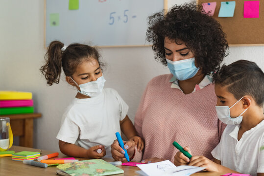Teacher with children wearing face mask in preschool classroom during corona virus pandemic - Healthcare and education concept
