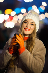 beautiful girl on the background of lights with coffee, on the street, holiday, new year. a walk through the evening city