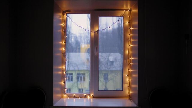 Winter decoration. Living Room at Christmas Eve. Window with Christmas lights. There is a beautiful fluffy snow outside the window