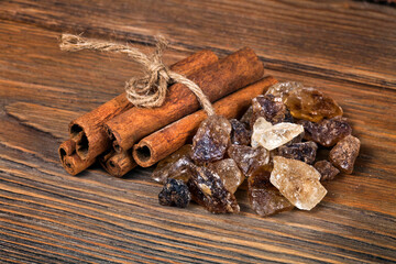 Stack of cinnamon sticks with crystals of brown sugar on a wooden background. Macro photography of spices.