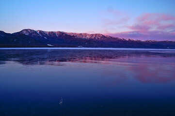 冬の湖の畔から見る夜明けの陽光に色づく山脈。