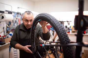 Fototapeta na wymiar mechanic fixing blue and white mountain bike wheel next to tool bench with mask
