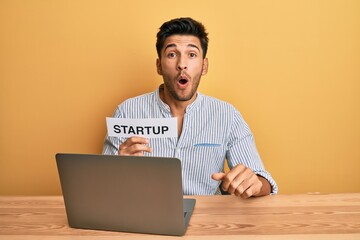 Young handsome man holding startup message as marketing development scared and amazed with open mouth for surprise, disbelief face