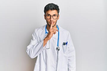 Young handsome man wearing doctor uniform and stethoscope asking to be quiet with finger on lips....