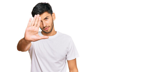 Young handsome man wearing casual white tshirt doing stop sing with palm of the hand. warning expression with negative and serious gesture on the face.