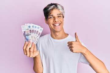 Young hispanic man holding russian 500 ruble banknotes smiling happy and positive, thumb up doing excellent and approval sign