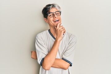 Young hispanic man wearing casual clothes and glasses looking confident at the camera with smile with crossed arms and hand raised on chin. thinking positive.