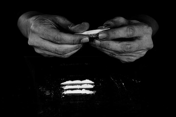 Drug addict man is preparing to snorting cocaine powder with rolled dollar banknote. Narcotics concept. Monochrome, black and white photo. Close-up macro shot. High resolution sharp photo. - obrazy, fototapety, plakaty