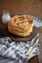 Fototapeta na wymiar Thin fried pancakes on a plate. Traditional food for Shrovetide. Pancake with sour cream on a wooden table.