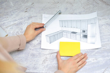On the table is a mock-up of a kitchen, an example of a palette of facades and drawer bodies and a handle for the door. girl orders furniture for the kitchen in the salon. Home improvement concept.