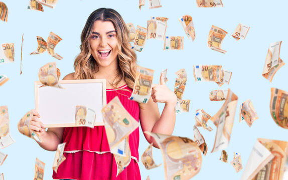Young caucasian woman holding empty white chalkboard pointing finger to one self smiling happy and proud