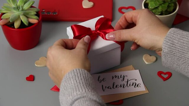 Somebody untie a bow on a valentine's day gift with message BE MY VALENTINE